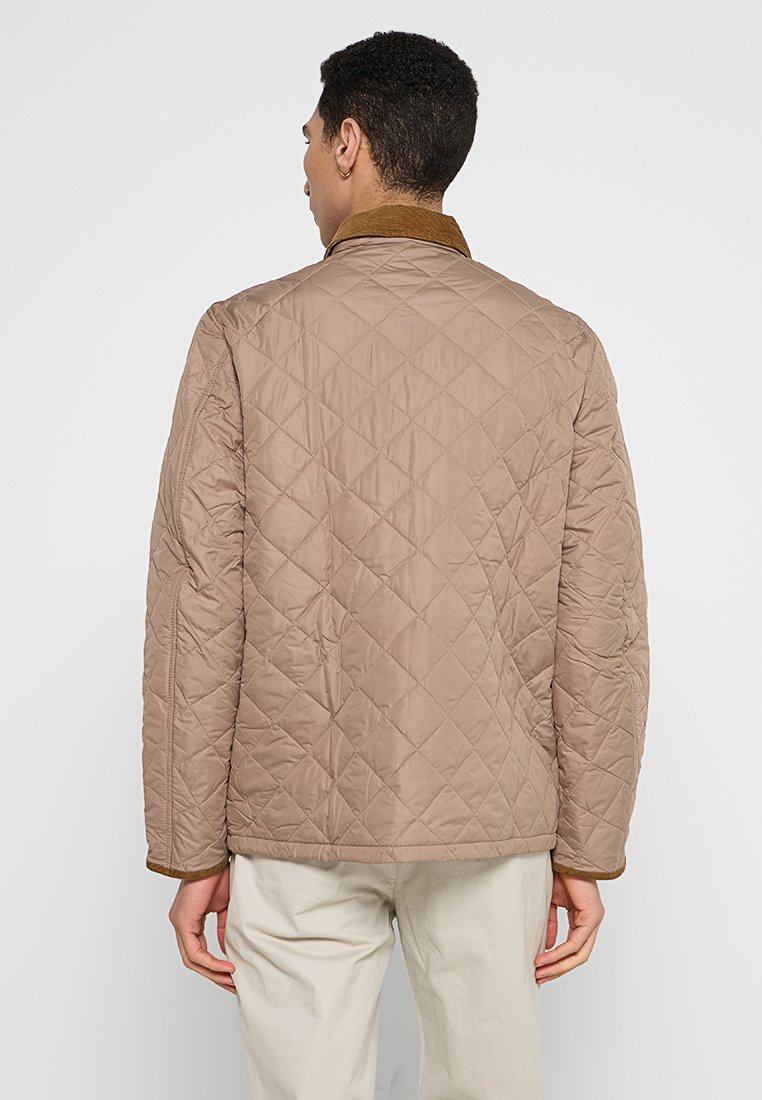 Veste matelassée beige avec un col brun, présentant un motif en losanges, des manches longues et une coupe droite. Design simpliste, matériau léger.
