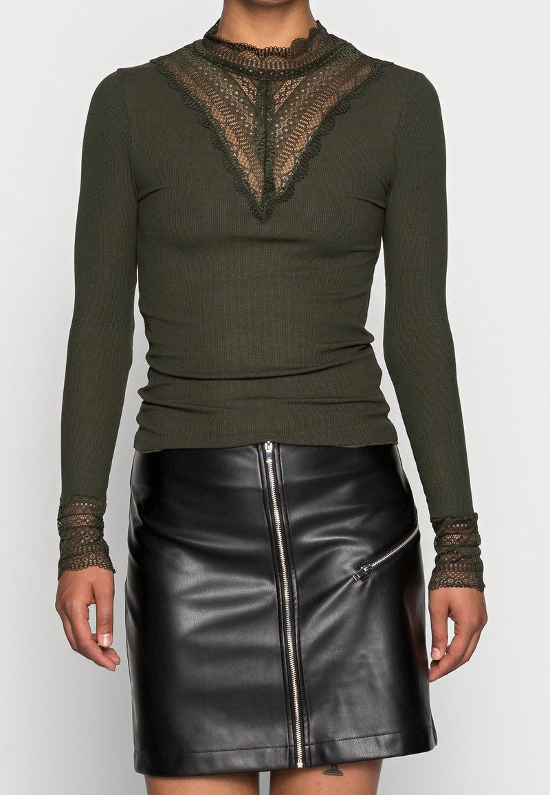 Olivgrön, ribbad långärmad topp med spetsdetaljer vid halsringning och ärmslut, matchad med en svart läder mini kjol med dragkedjor.