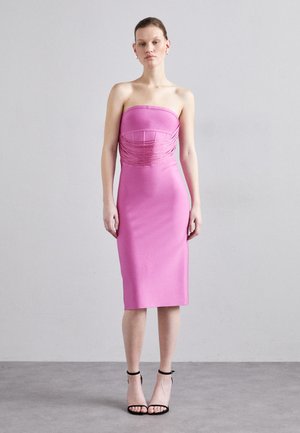 Strapless roze bodycon jurk met geplooide stofdetails bij de buste, gladde textuur, knielang, gecombineerd met zwarte sandalen met bandjes.
