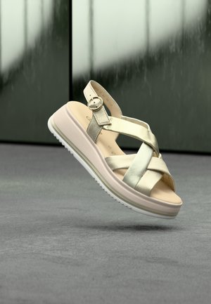 Sandales à brides avec des lanières métalliques argentées, une semelle intérieure beige rembourrée et une semelle extérieure blanche, ornées d'une boucle ronde.