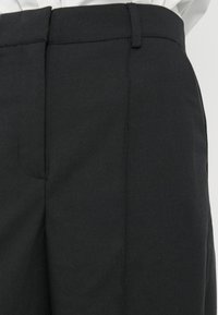 Pantaloni negri cu textură netedă, prevăzuți cu față plată, găici pentru curea și pliuri bine călcate. Design simplu și funcțional.