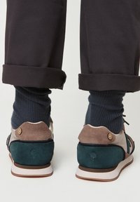 Bunte Sneakers bestehen aus einer Mischung aus Wild- und Glattleder in Dunkelgrün, Beige und Braun. Gummisohle, Schnürdesign und Knopfdetails.