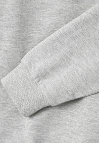 Material de sudadera de color gris claro con una textura suave; presenta un puño acanalado y un sutil patrón jaspeado. Vista en primer plano del detalle de la manga.