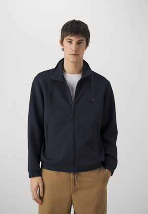 Giacca zip-up blu navale in un morbido tessuto testurizzato con colletto alto, dotata di due tasche frontali e cordini regolabili.