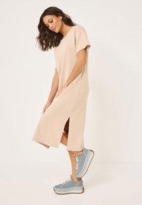 Beige midi-klänning med korta ärmar och sidofickor, tillsammans med ljusgrå sneakers med tjock vit sula och brun trädd.