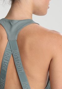 Grijze sporttop met X-rugdesign, voorzien van reliëf "JUST DO IT" branding op de banden, met een gladde textuur en huid zichtbaar erachter.
