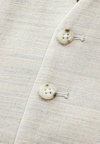 Tissu beige avec un motif texturé subtil, présentant deux boutons ronds de couleur claire cousus à l'avant.