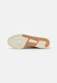 Sole obuvi Adidas s texturovaným gumovým povrchem, krémová barva s oranžovými akcenty. Výrazný vzor podrážky pro přilnavost.