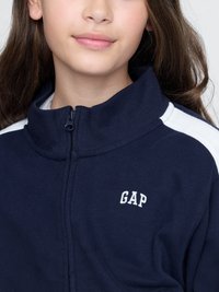 Námornícka zipová bunda s bielymi ramennými akcentmi, s bielym logom "GAP" na ľavej strane hrude. Mäkka tkanina, vysoký golier.