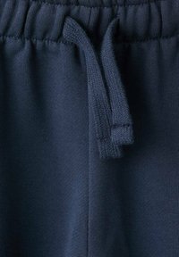Mørkeblå sweatpants i blødt stof, med elastisk talje og snoretræk samt en struktureret finish. Nærbillede af detaljer på taljen.