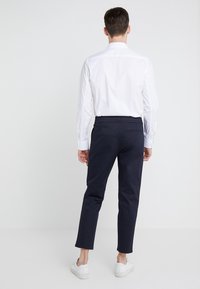 Biała koszula z długim rękawem i kołnierzykiem, połączona z granatowymi, dopasowanymi spodniami oraz białymi sneakersami, z tylną kieszenią jako detal.