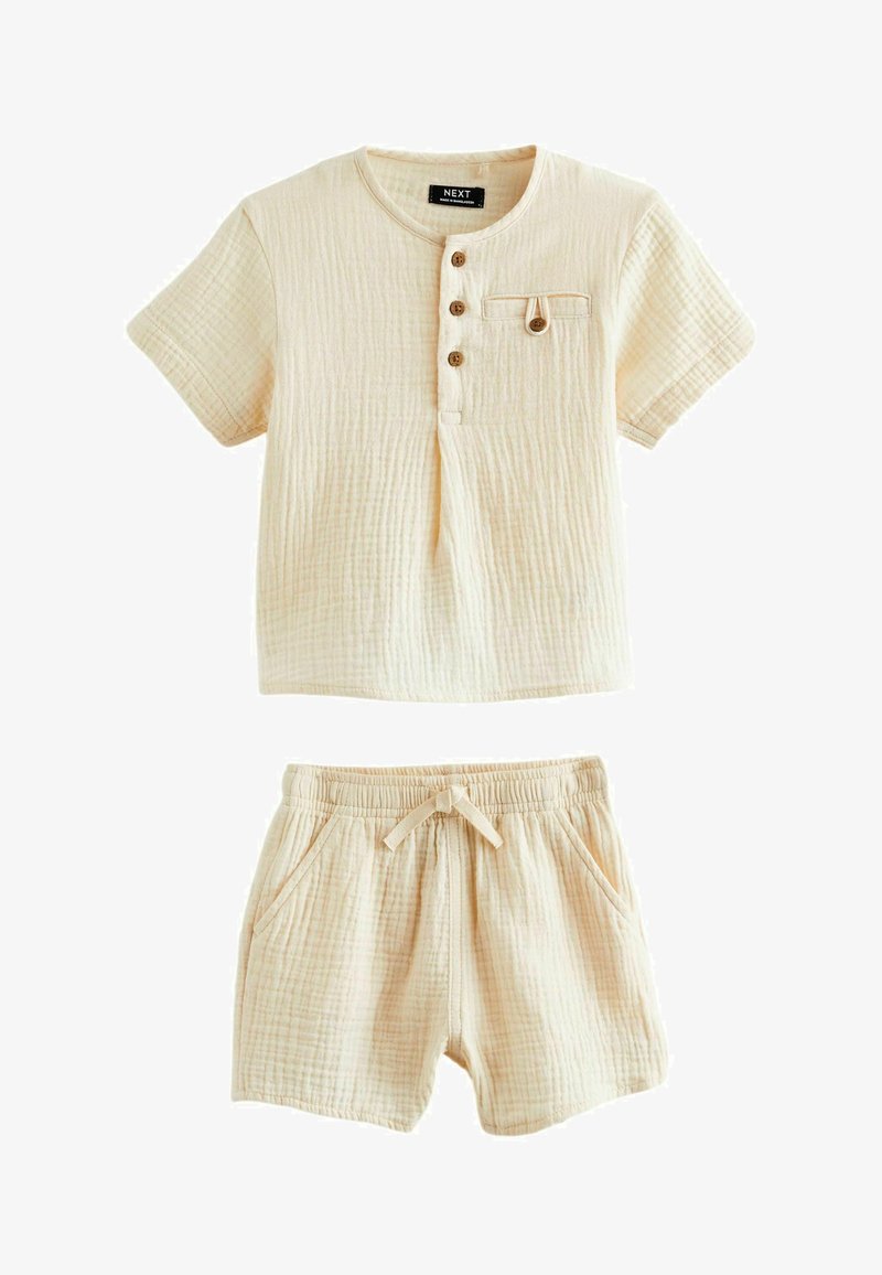 Conjunto de loungewear de algodón color beige claro que incluye una camiseta henley de manga corta con tres botones y un bolsillo, combinada con pantalones cortos de cintura elástica.