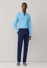 Camisa de botones azul claro, pantalones azul oscuro y alpargatas azules. La camisa tiene cuello y un pequeño bolsillo en el pecho.