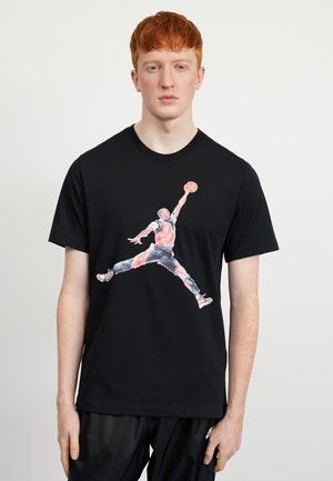 T-shirt nera a maniche corte con una grafica di un giocatore di basket che salta per tirare, in stile acquerello, con colori a contrasto.