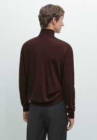 Burgundyröd långärmad tröja med hög krage, med en mjuk textur, avslappnad passform och ribbade muddar. Buren med mörkgrå byxor.