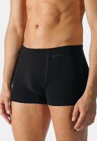 Boxer da uomo in cotone nero con design aderente, caratterizzati da una vita elasticizzata e dettagli di cucitura. Il tessuto appare liscio ed elastico.
