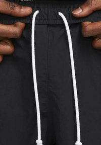 Black swim shorts with an elastic waistband, featuring a white drawstring for adjustment. Smooth texture, simple design, no visible patterns.