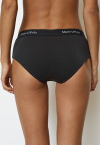 Sous-vêtements hipster en coton noir avec une ceinture élastique arborant le logo "Marc O'Polo". Texture lisse, design minimaliste et forme couvrante.