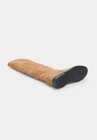 Bota de ante marrón hasta la rodilla con suela de goma negra plana, que presenta una textura suave y un diseño de punta redondeada.