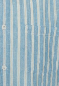 Blauw-wit gestreepte linnen shirt met een patchzak en een voorkant met knoopsluiting met twee knopen. Getextureerde, lichte stof.