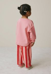 Pink sweatshirt with dropped shoulders, paired with pink and red striped wide-leg pants. Notable clips in hair. Casual, comfortable fit.