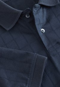 Mornarsko modra polo majica iz teksturirane tkanine z diamantnim vzorcem, kratkimi rokavi in ovratnikom z gumbi, ki ga krasi srebrni gumb.