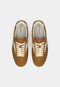 Par brune og kremfargede Karl Lagerfeld-sneakers med hvite lisser, sett ovenfra på en hvit bakgrunn.