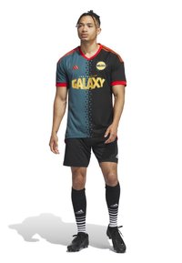 Zwart en groenblauw voetbalshirt met rode accenten, voorzien van het "GALAXY"-logo, sterpatroon en korte mouwen, gecombineerd met zwarte shorts en gestreepte sokken.
