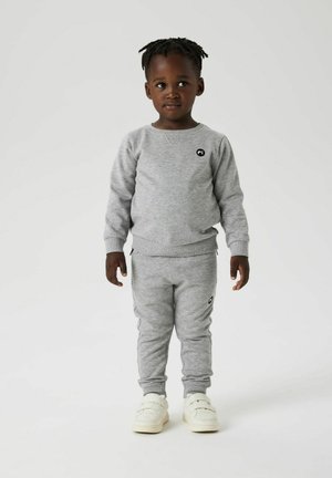 Ensemble de sweatshirt gris et de pantalon de survêtement, fabriqué en tissu doux. Présente un petit logo noir sur la poitrine et des accents de poche latérale. Baskets blanches.