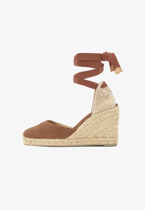Chaussure compensée espadrille en toile marron avec semelle en jute tressée et liens à nouer autour de la cheville avec embouts métalliques.