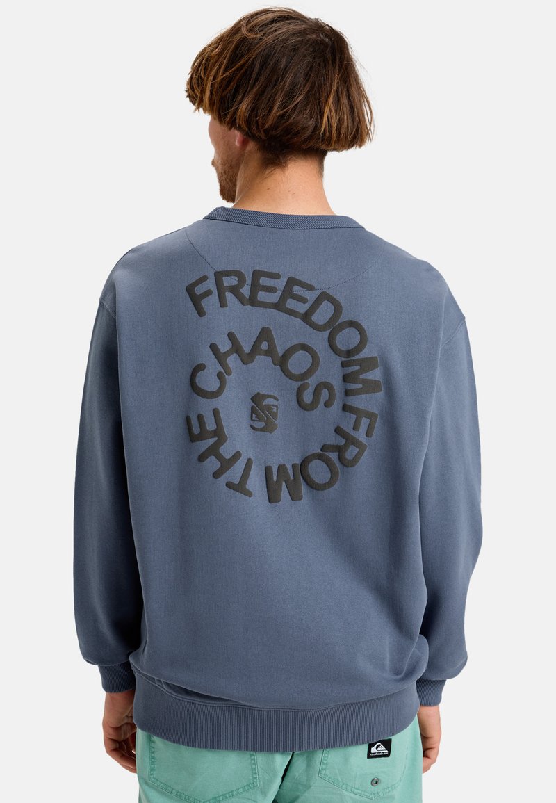 Felpa blu con scollo rotondo e polsini a costine, caratterizzata da un design grafico circolare di testo nero sulla schiena e un'etichetta con logo sull'orlo.