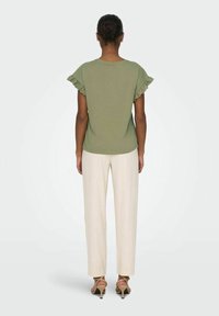 Olivgrön t-shirt med volangärmar, kombinerad med krämfärgade byxor och beige klackar, sedd bakifrån.