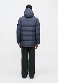 Μπλε �φουσκωτό μπουφάν με κουκούλα, που διαθέτει καπιτονέ σχέδιο, ριγέ τελείωμα και πλαϊνές τσέπες. Συνδυάζεται με χαλαρούς σκούρους παντελόνες.