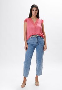 Top senza maniche rosa con bordi in pizzo, texture a pois, abbinato a jeans a vita alta di colore blu chiaro e sandali beige con punta aperta.