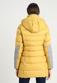 Gelbe Pufferjacke mit Kapuze, ausgestattet mit grauen Stoffakzenten an den Ärmeln und gerippten Bündchen. Geplottetes Design, mittellange Länge.