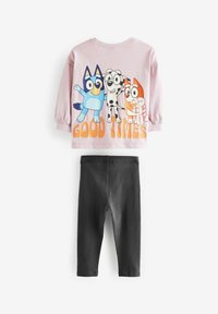 Rosa Langarmshirt mit animierten Hundekarikaturen und dem Text "GUTE ZEITEN". Kombiniert mit schwarzen Baumwollleggings, die einen figurbetonten Schnitt haben.