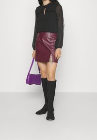 Svart genomskinlig blus med volangkrage, vinröd fusk-läderkjol med sida slits, svarta knähöga stövlar och en liten lila handväska med krokodilprägling.