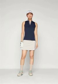 Mornarsko modra brezrokavna golf polo majica z zadrgo in belimi poudarki, v kombinaciji s svetlo bež golf krilom. Nosi se z belo kapo in rokavico.