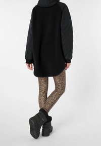 Giacca nera in pile con cappuccio trapuntato e maniche lunghe, abbinata a leggings beige con stampa leopardata e stivali neri foderati in pelliccia.