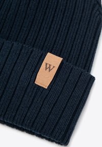 Cappellino in maglia a coste blu navy con risvolto e etichetta rettangolare in pelle marrone con la lettera "W". Texture liscia e vestibilità aderente.