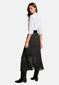 Jupe maxi à pois noirs avec une superposition en tulle, assortie à une chemise blanche à boutons et des bottes noires montantes.