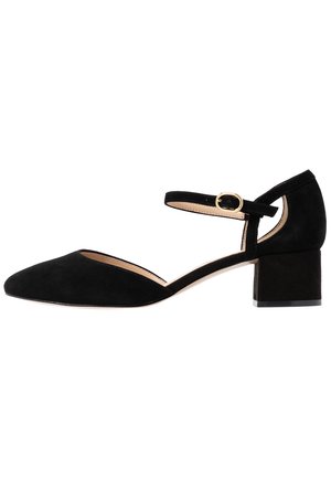 Zwarte suède pump met een spitse neus, verstelbare enkelband, gouden accenten en een vierkante middenheck. Bevat een uitsparing aan de zijkant.