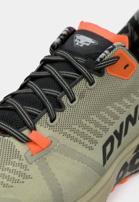 Παπούτσια trail running σε ανοιχτό γκρι με μαύρο δίχτυ, διακοσμημένα με πορτοκαλί λεπτομέρειες. Διαθέτουν δυναμικό σύστημα δέσιμο και τυπωμένη, μαξιλάρα σόλα.