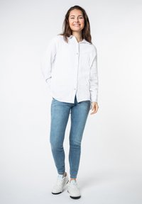 White button-up shirt with textured fabric, paired with blue slim jeans and white sneakers, featuring colored accents on the shoe.