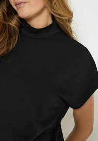 Sort mock turtleneck top med korte ærmer, lavet af glat, strækbart materiale. Rene linjer og minimalistisk design, velegnet til forskellige outfits.