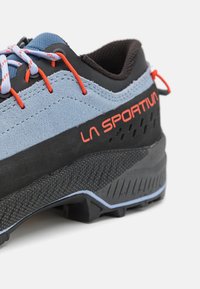 Pantof de escaladă din suede albastru și material sintetic negru, cu accente roșii, talpă din cauciuc texturat și călcâi întărit. Logo-ul "La Sportiva" este vizibil.