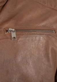 Braune Lederjacke mit einer horizontalen Reißverschlusstasche und einem silbernen Reißverschluss. Die Textur ist glatt mit einem leichten Glanz. Nähte sind sichtbar.