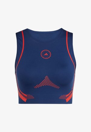 Sportski grudnjak tamnoplave boje s crvenim akcentima. Ima okrugli logotip, glatku teksturu i dijagonalne prugaste uzorke sa strane.