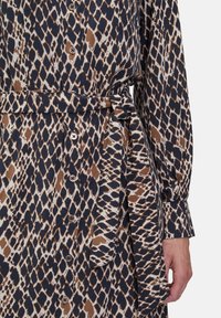 Sukienka zapinana na guziki w brązowy, granatowy i biały wzór zwierzęcy. Posiada pasek w talii do zawiązania oraz długie rękawy z guzikami na mankietach.