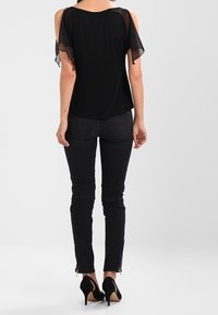 Černý top s průhlednými krátkými rukávy, spojený s černými slim fit džíny s zipy na kotnících. Nosit s černými vysokými podpatky.